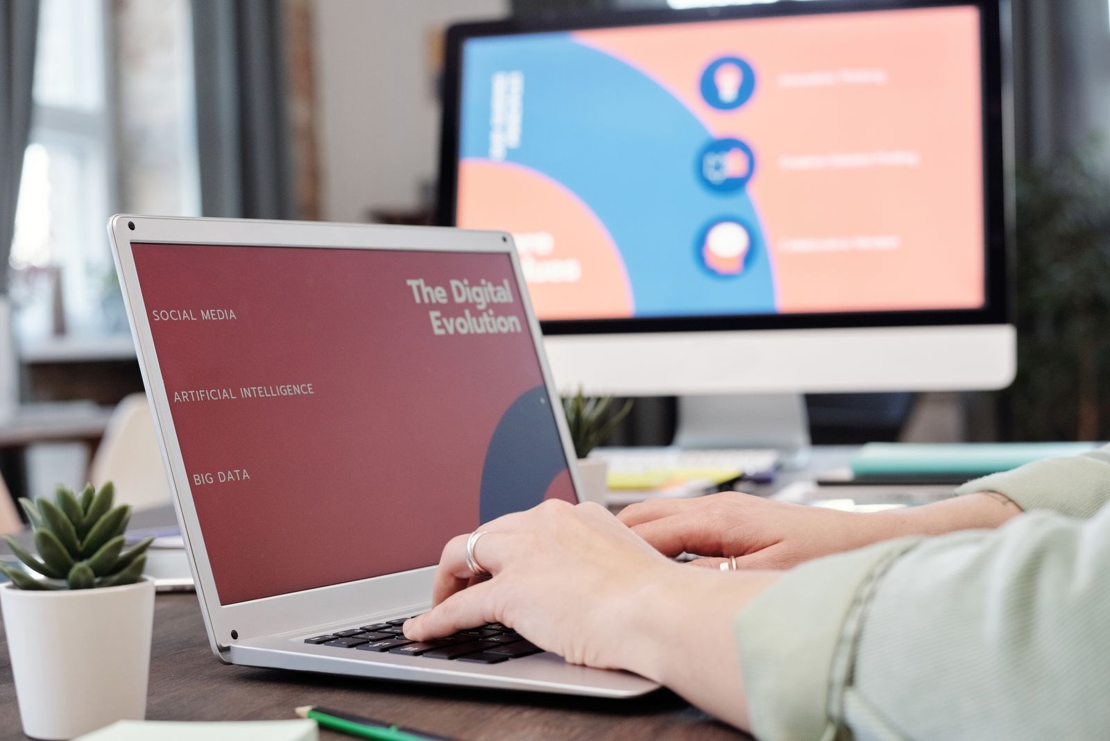 Person typing on a laptop with a data and analytics presentation showing on a second monitor